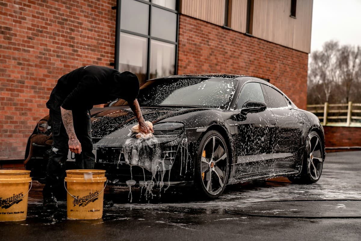 Detailer carefully hand-washing a dark Porsche with foam